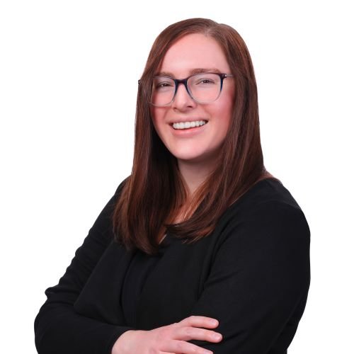 A woman with long straight brown hair, glasses, smiling, wearing a black top, crossed arms, against a white background.