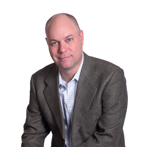 A man with a bald head and blue eyes wearing a checkered blazer and a white shirt, posing against a white background.